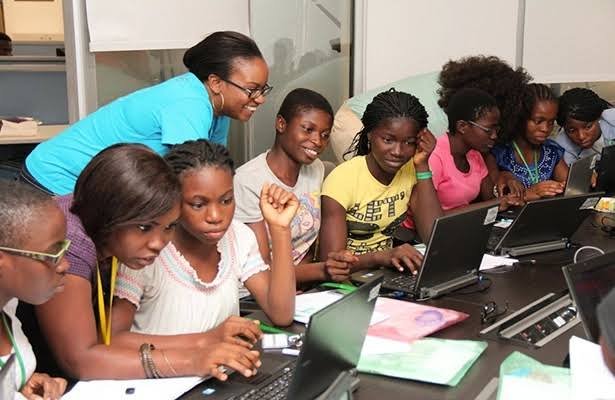 Girls learning together on laptops with a mentor guiding them