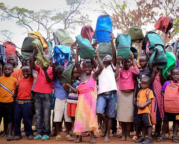 Children cheerfully holding up new school backpacks