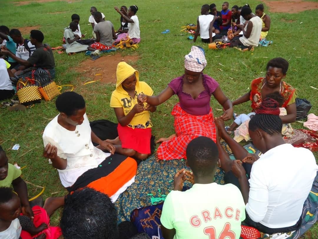 Women and girls learning beadwork together on the grass